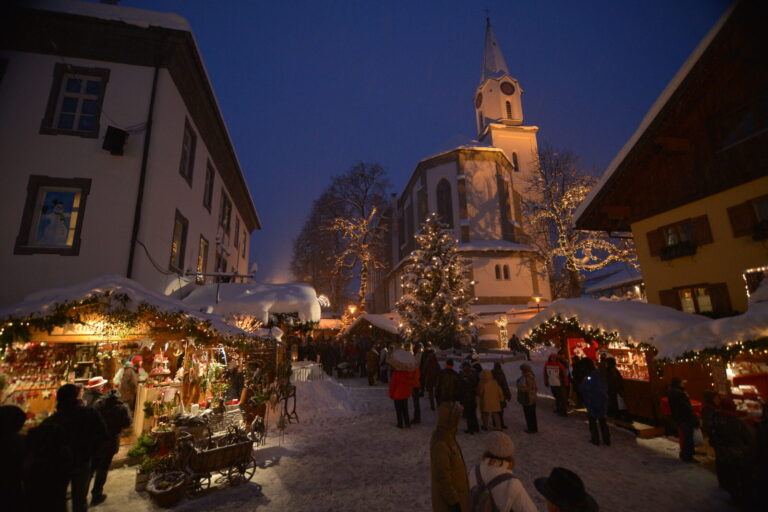 Erlebnis-Weihnachtsmarkt Bad Hindelang am Abend: beleuchtete Hütten im Schnee