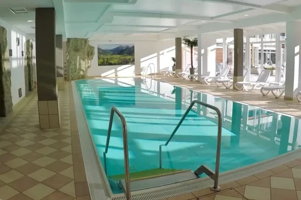 Heller Innenpool der Ferienanlage Die Gams in Bad Hindelang im Allgäu mit Liegestühlen, großen Fensterfronten und entspannter Wellnessatmosphäre.