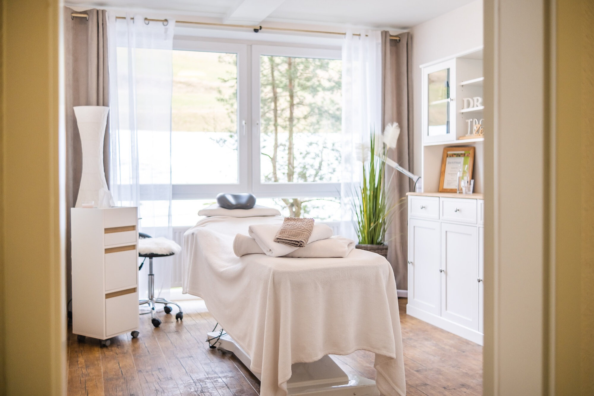 Lichtdurchfluteter Massageraum der Ferienanlage Die Gams in Bad Hindelang im Allgäu mit Wellnessliege, Handtüchern und stilvollem Ambiente.
